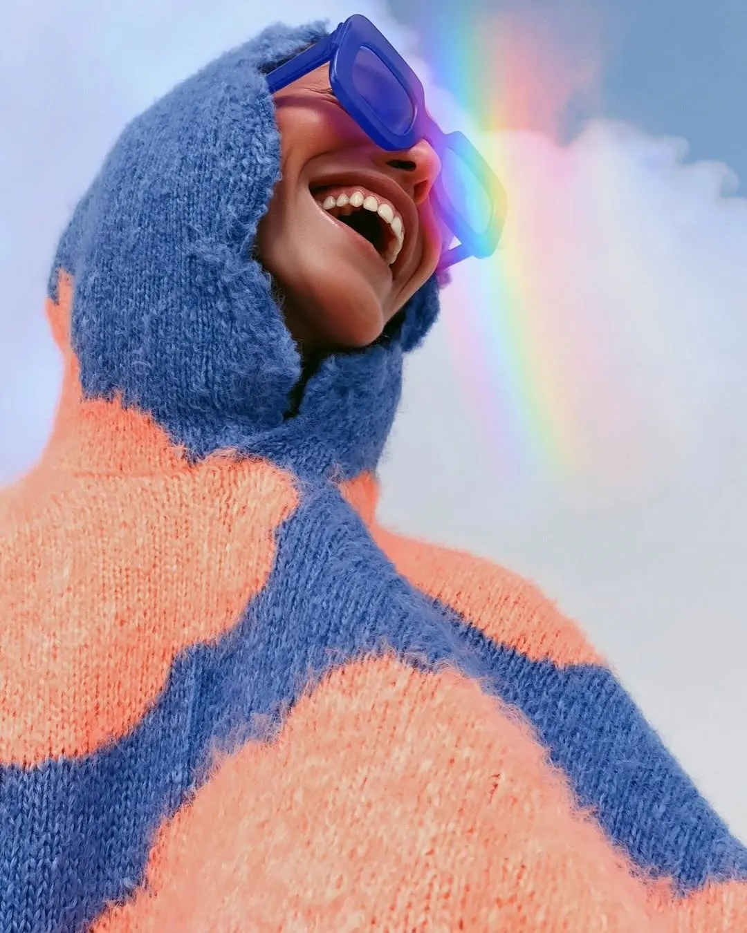 Laughing model in a blue fur hood under a rainbow of light, with a floral face painting